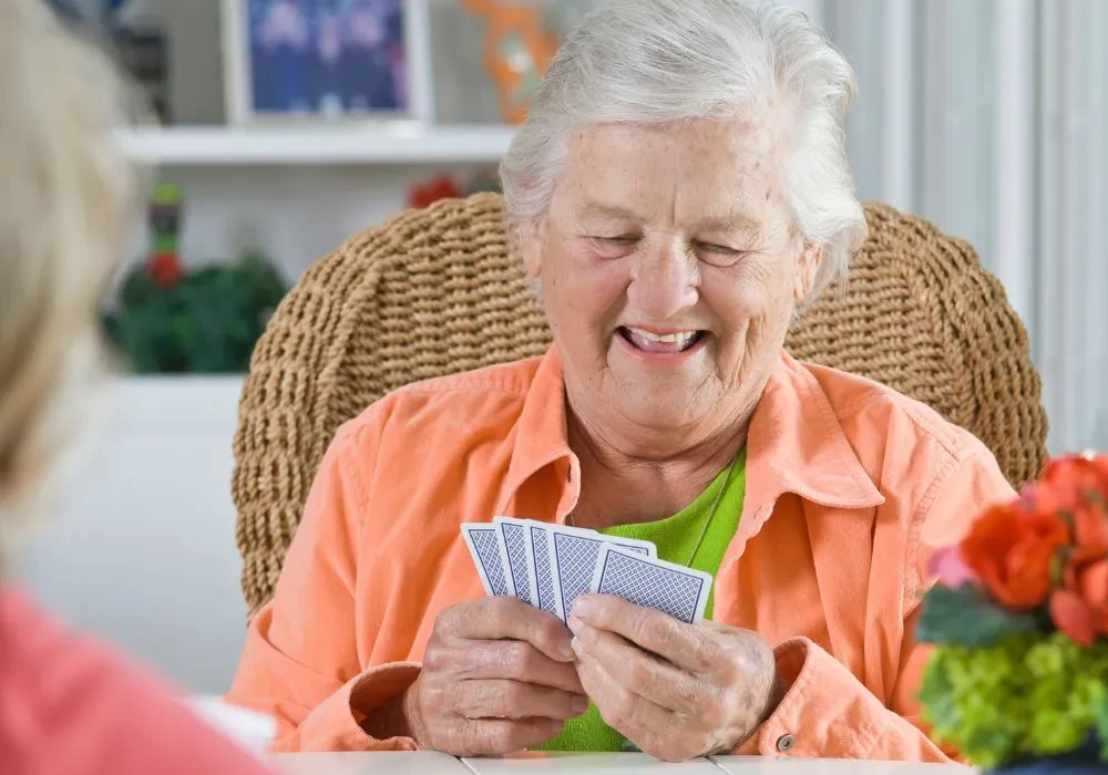 A female senior citizen laughing while playing cards so she can stay mentally sharp in retirement