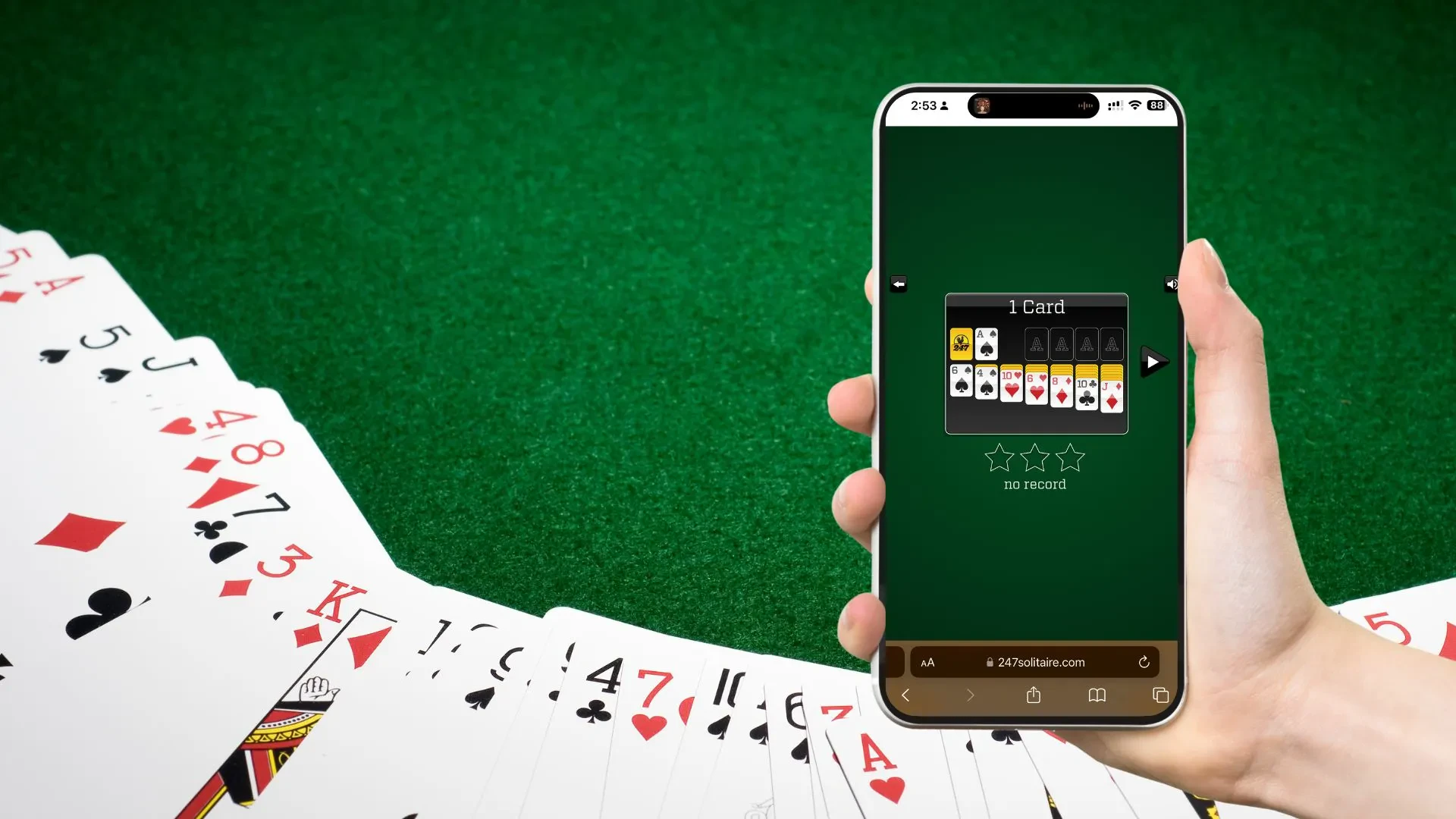 A deck of cards are spread out on a green background. A hand is holding a phone with its screen displaying a game of solitaire from the 247 solitaire website