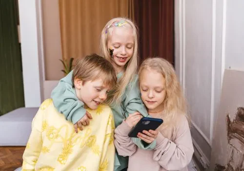 Three kids laughing over a mobile game one of them is playing